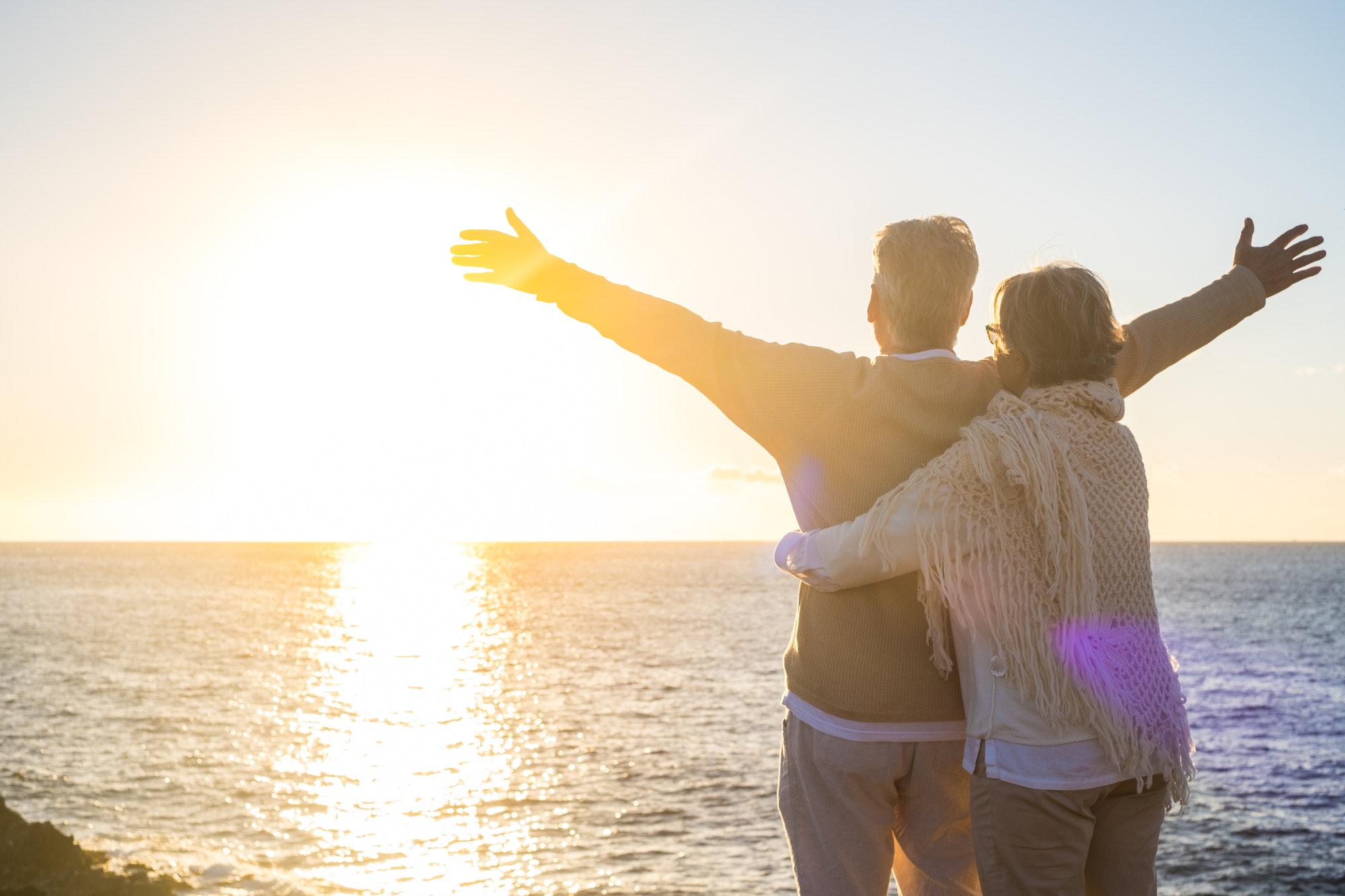 couple of two happy senior ad mature old people at the beach looking at the sea and the sun